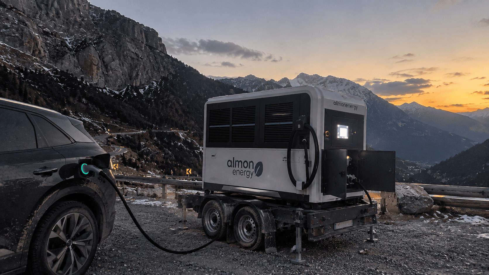 Mobiler Batterie-Energiespeicher von Almon Energy auf einem PKW-Anhänger lädt ein Elektro-SUV an einer abgelegenen Bergstraße vor verschneiten Alpengipfeln bei Sonnenuntergang.
